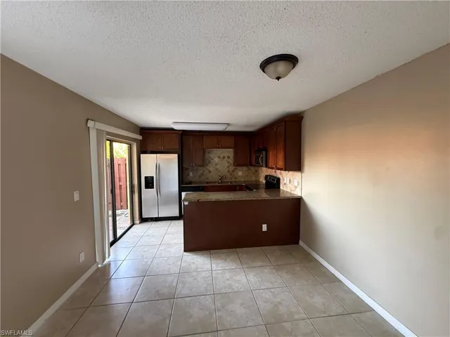 Kitchen with dark wood finish cabinetry, a peninsula, stainless steel appliances, light tile patterned floors, and a textured ceiling