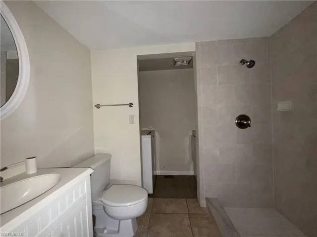 Bathroom featuring vanity, a tile shower, light tile patterned flooring, and washer / clothes dryer