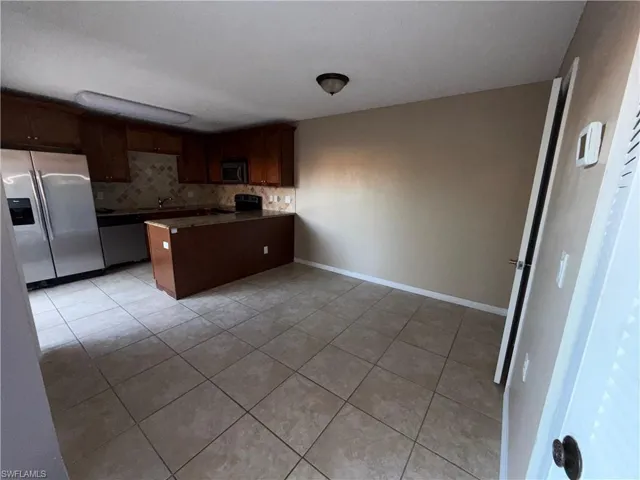 Kitchen with a peninsula, stainless steel appliances, dark wood finish cabinets, light tile patterned flooring, and tasteful backsplash