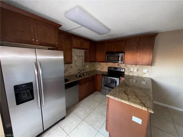 Kitchen with stainless steel appliances, dark stone countertops, a peninsula, light tile patterned floors, and a textured ceiling