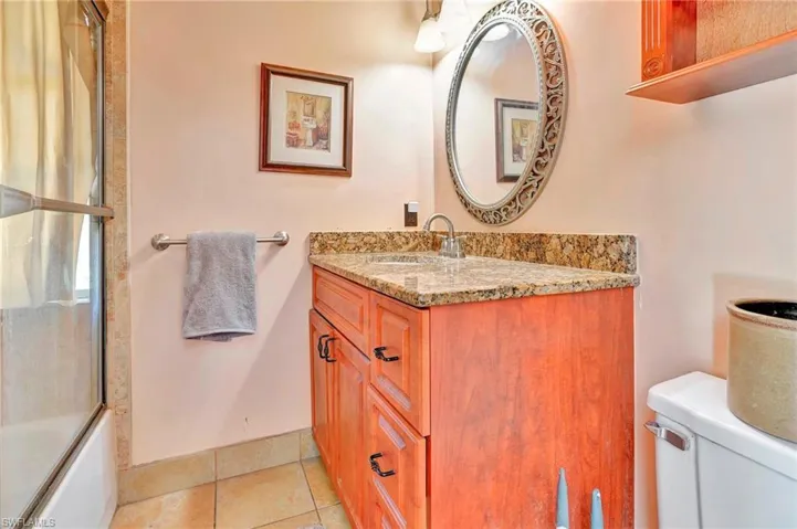 Full bathroom with tile flooring, vanity with extensive cabinet space, toilet, and bath / shower combo with glass door