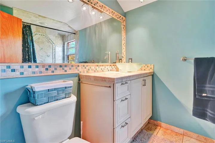 Bathroom with tile flooring, vaulted ceiling, backsplash, vanity, and toilet