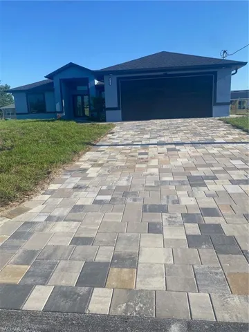 View of front of house with roof with shingles, stucco siding, decorative driveway, a front yard, and a garage