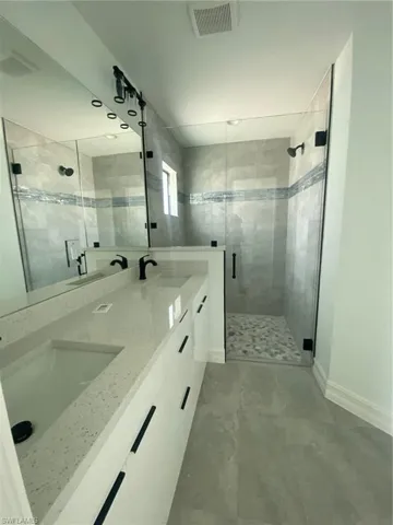Full bathroom with a shower stall, baseboards, and double vanity