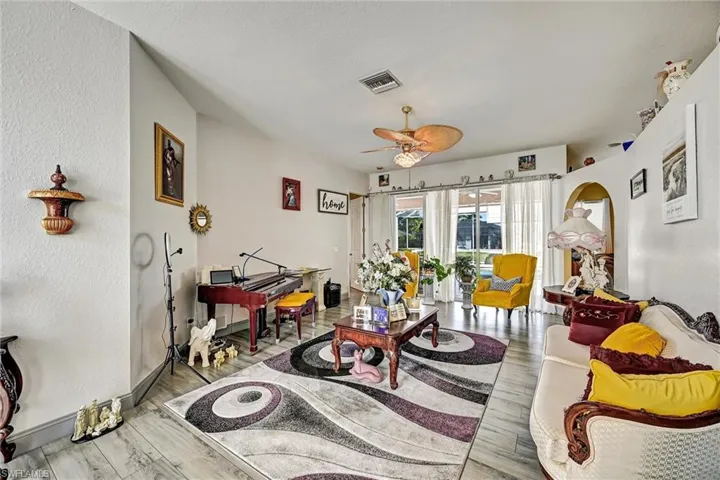 Living room featuring arched walkways, wood style tile floors, and a ceiling fan. Sliding glass doors to the lanai.