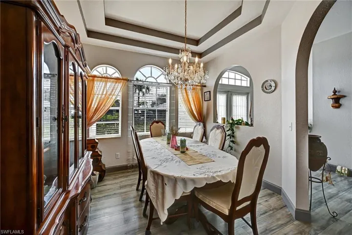 Dining area featuring arched walkways, a chandelier, wood style tile floors, and a raised ceiling