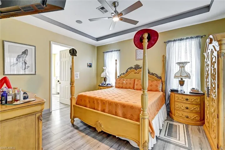 Primary Bedroom with a tray ceiling, multiple windows, wood style tile finished floors, and ceiling fan