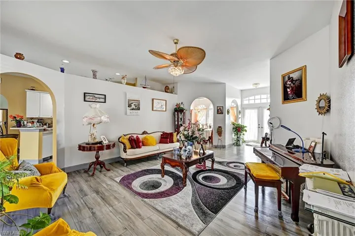 Living room featuring arched walkways, wood style tile floors, and a ceiling fan. Double French entry doors.