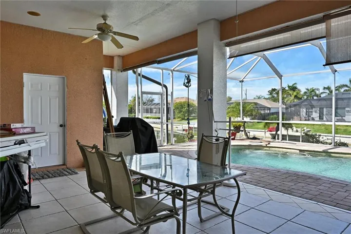 Patio dining space with a screened lanai, ceiling fan, light tile patterned tile floors overlooking free-form shaped pool