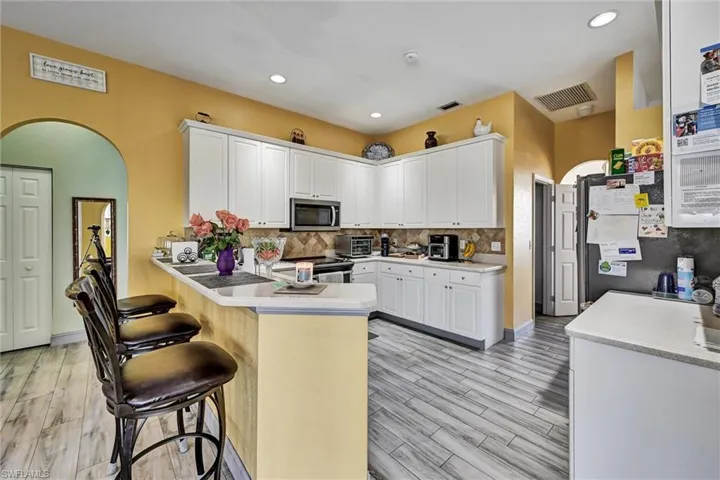 Kitchen with arched walkways, a peninsula, white cabinets, wood-style tile flooring, and recessed lighting