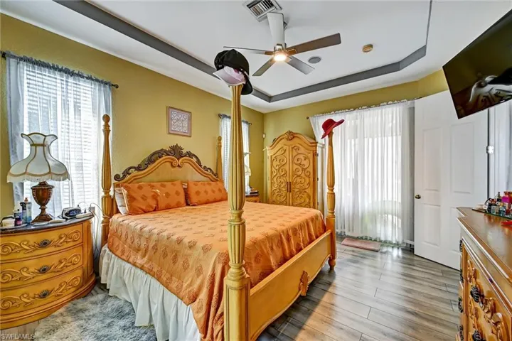 Primary Bedroom with a tray ceiling, multiple windows, wood style tile finished floors, and ceiling fan