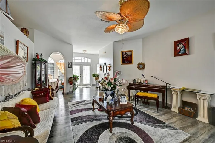 Living room featuring arched walkways, wood style tile floors, and a ceiling fan. Double French entry doors.