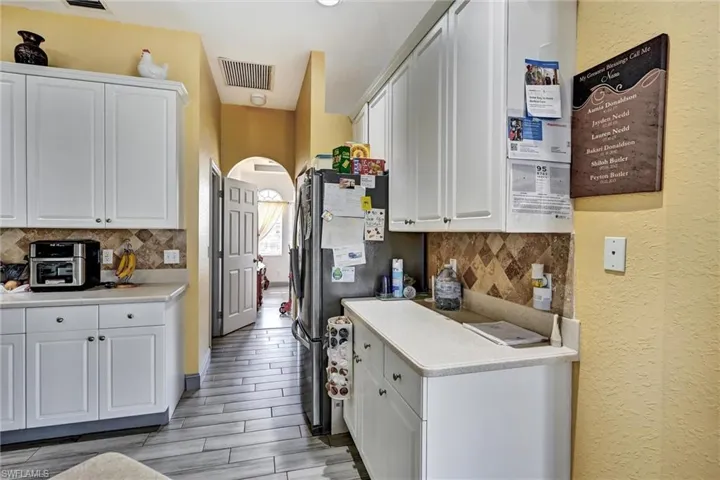 Kitchen with arched walkways, white cabinetry, freestanding refrigerator, and wood style tile floors