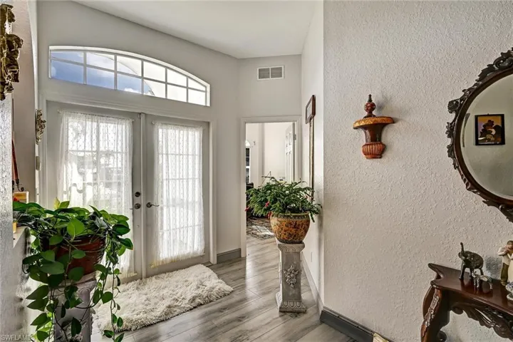 Entryway featuring a textured wall, wood style tile floors, French entry doors, and a high ceiling. A peek towards the den/office.