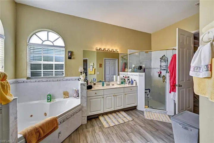 Full bath with 2 vanities, an oversized garden bathtub, and wood style tile floors, jetted tub, and shower stall