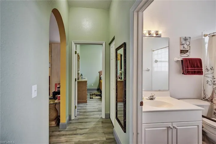 Hallway and full guest bath featuring vanity, shower / bath combo with shower curtain, and light wood style tile floors