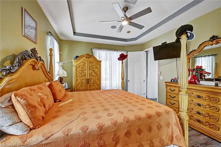 Primary Bedroom with a tray ceiling, multiple windows, wood style tile finished floors, and ceiling fan