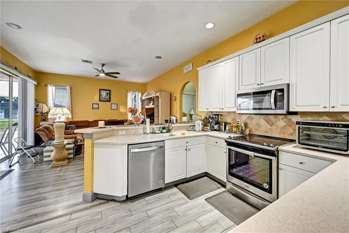Kitchen featuring white cabinets, stainless steel appliances, open floor plan, a breakfast bar peninsula, and recessed lighting. Looking towards the family room