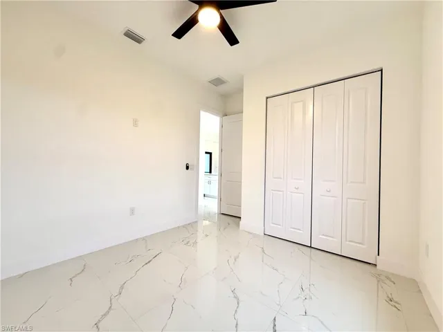 Unfurnished bedroom with a closet, light marble finish floors, and ceiling fan