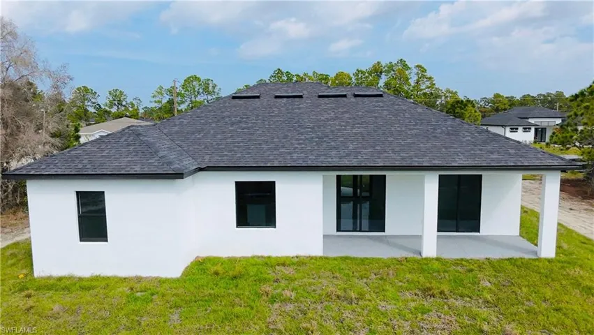 Back of property with a yard, stucco siding, and a shingled roof
