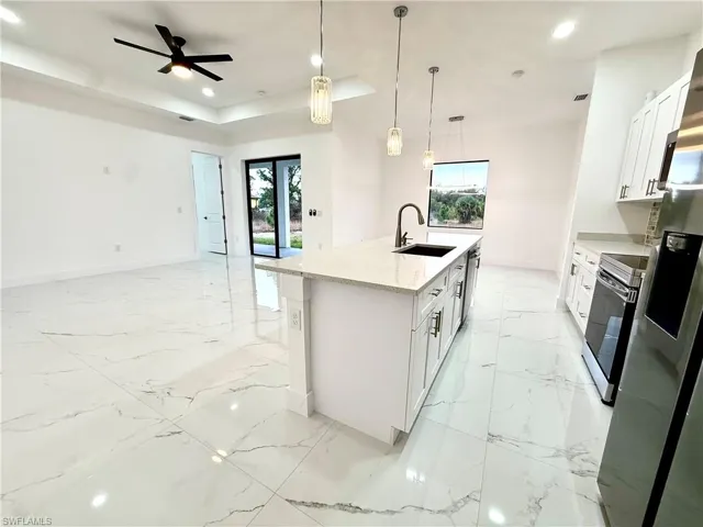 Kitchen featuring white cabinets, hanging light fixtures, an island with sink, light stone countertops, and a tray ceiling
