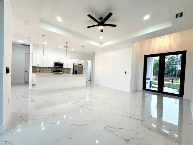 Unfurnished living room with ceiling fan, a raised ceiling, and recessed lighting