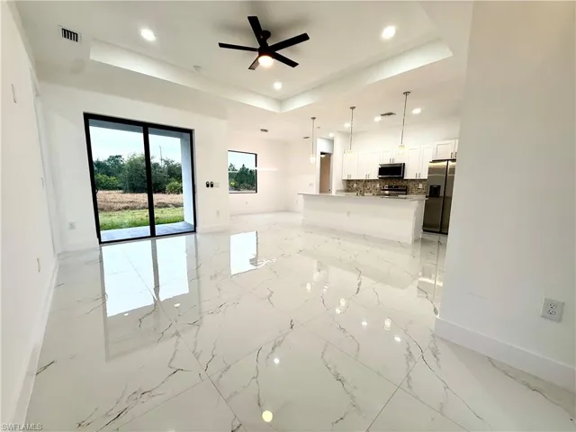 Unfurnished living room with a ceiling fan, a raised ceiling, recessed lighting, and light marble finish flooring