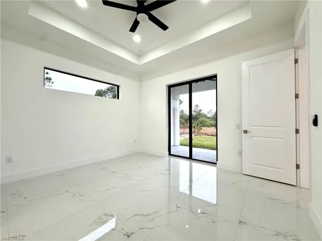 Spare room with a tray ceiling, healthy amount of natural light, recessed lighting, a ceiling fan, and light marble finish floors