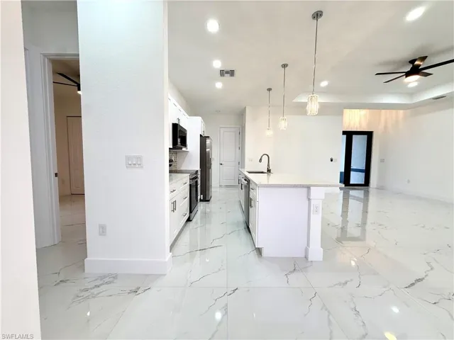 Kitchen featuring a ceiling fan, white cabinetry, stainless steel appliances, hanging light fixtures, and a tray ceiling