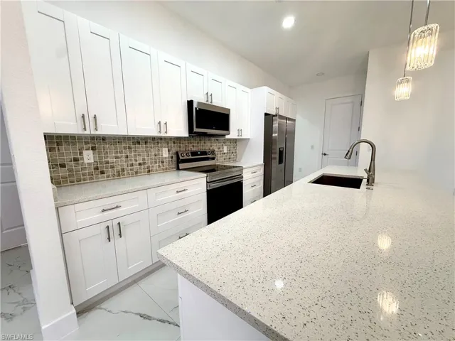 Kitchen featuring stainless steel appliances, light stone countertops, white cabinets, backsplash, and light marble finish floors