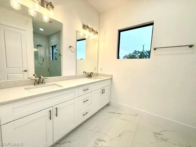 Bathroom featuring a marble finish shower, double vanity, light marble finish floors, and a textured wall