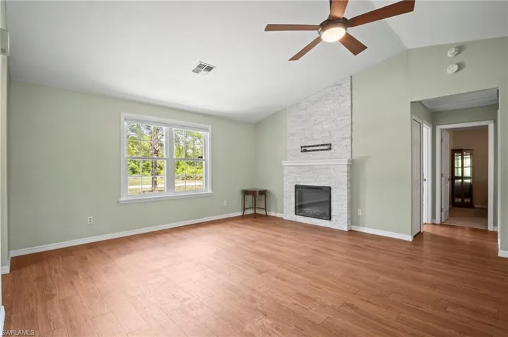 Unfurnished living room with ceiling fan, healthy amount of natural light, lofted ceiling, a stone fireplace, and wood finished floors