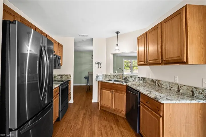 Kitchen with black appliances, a sink, wood finished floors, and brown cabinets
