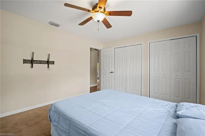 Carpeted bedroom with two closets, baseboards, and a ceiling fan