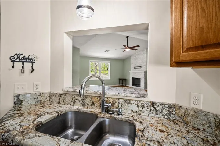 Kitchen view of a sink, a ceiling fan, light stone countertops, brown cabinetry, and a fireplace