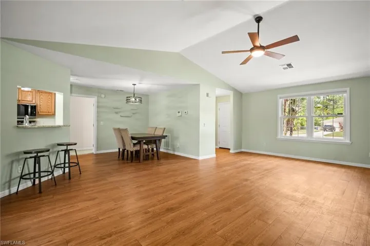 Living area with a ceiling fan, light wood-style flooring, vaulted ceiling, and baseboards