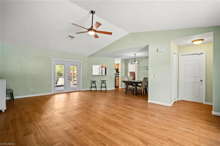 Living room with lofted ceiling, a ceiling fan, light wood-type flooring, french doors, and baseboards