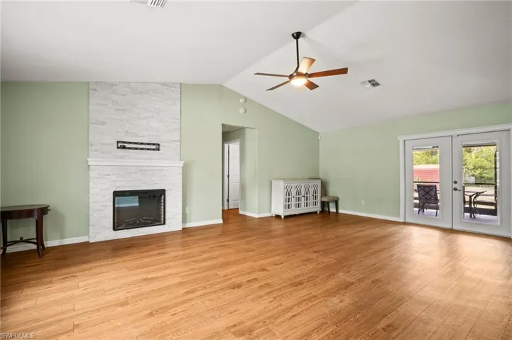 Unfurnished living room with a ceiling fan, wood finished floors, a stone fireplace, french doors, and high vaulted ceiling