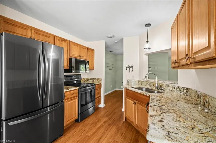 Kitchen with appliances with stainless steel finishes, a sink, light wood-style flooring, and brown cabinetry