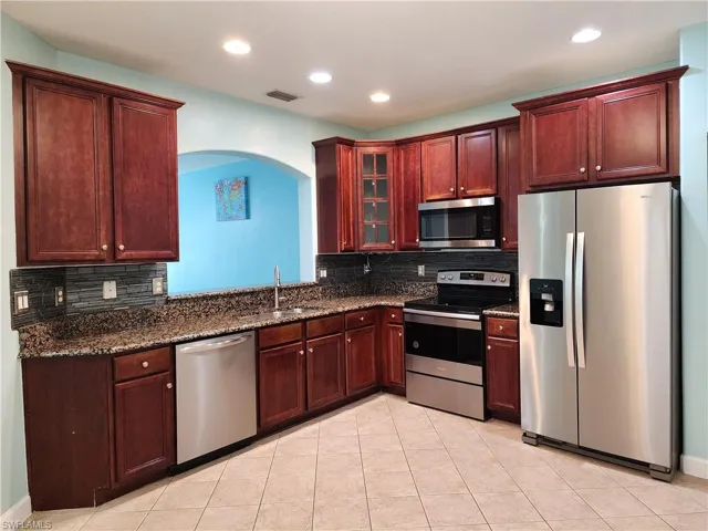 Kitchen featuring backsplash, tall cabinets, tile floors, stainless steel appliances, and serving window