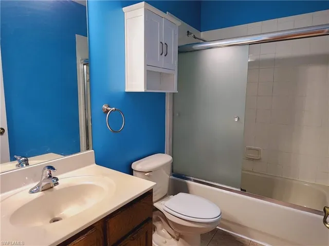 Full bathroom featuring tile flooring, combined bath / shower with glass door, toilet, and vanity
