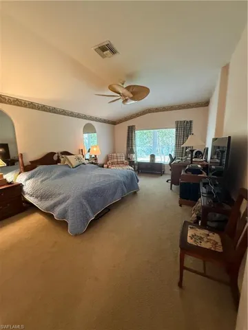This expansive room features vaulted ceilings, a ceiling fan, and large windows providing views of the outdoors