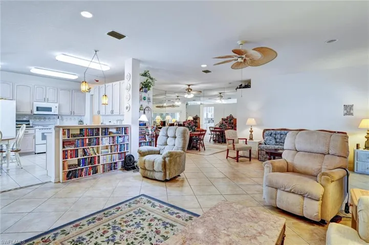 Open-concept living area featuring tile flooring, white kitchen cabinetry with pendant lighting, a built-in bookshelf island, and a ceiling fan
