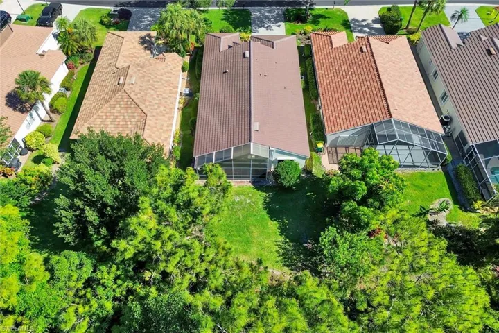 Aerial perspective showcasing a property with a brown shingle roof, green lawn space, and mature trees