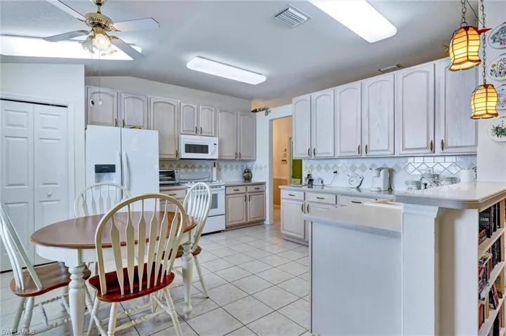 Kitchen featuring white cabinetry, tile flooring, white appliances, and a built-in breakfast bar