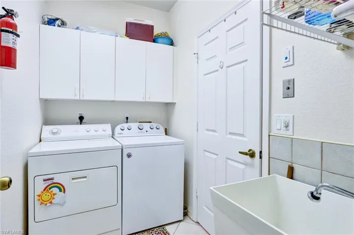 Dedicated laundry area featuring white wall cabinetry, a utility sink, and tiled flooring