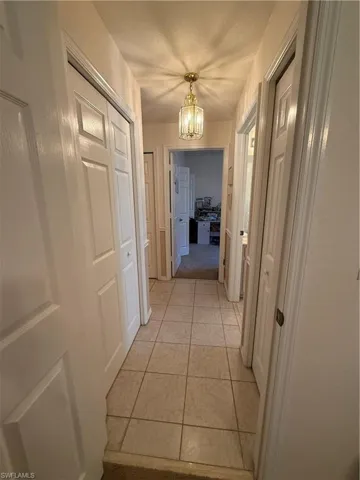 Hallway featuring tile flooring, a brass-toned ceiling fixture, and white paneled doors