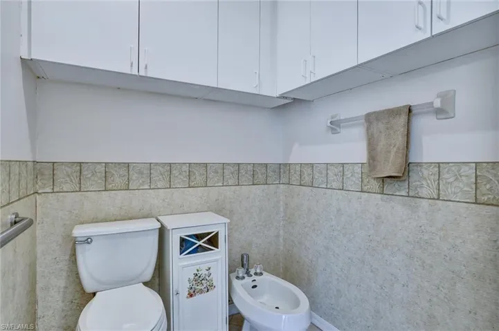 Bathroom featuring extensive white overhead cabinetry, a white toilet, and a bidet