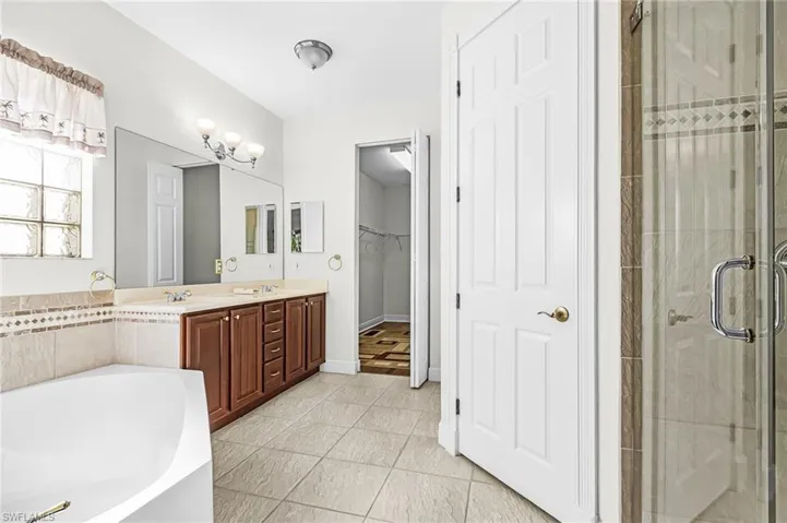 Bathroom with double vanity, a stall shower, a bath, a walk in closet, and light tile patterned flooring