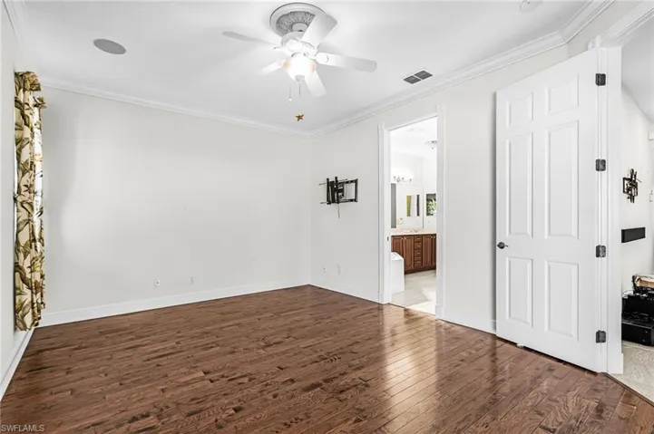 Unfurnished bedroom featuring crown molding, dark wood-type flooring, a ceiling fan, and ensuite bathroom